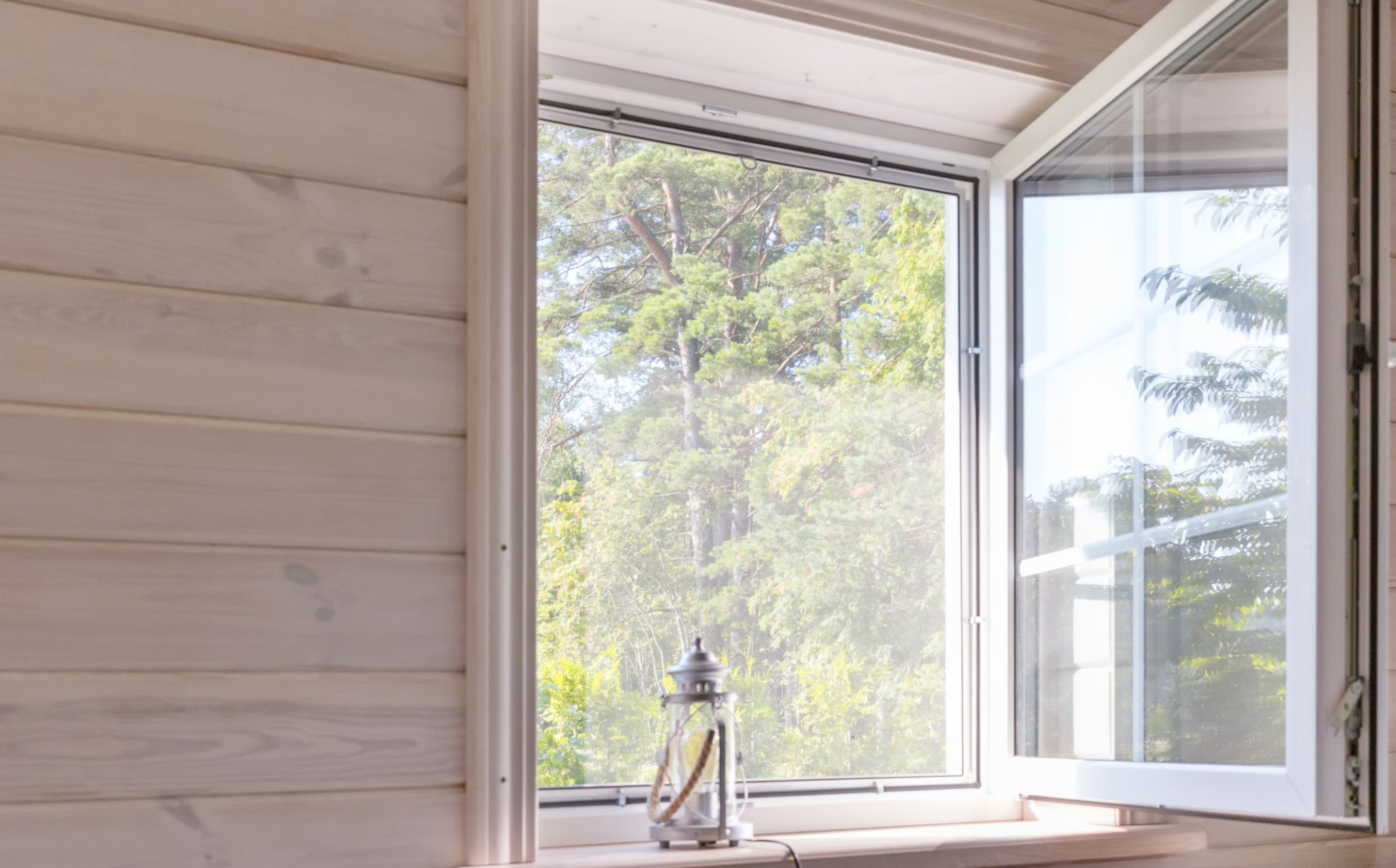 window open showing trees outside and small lantern on window sill