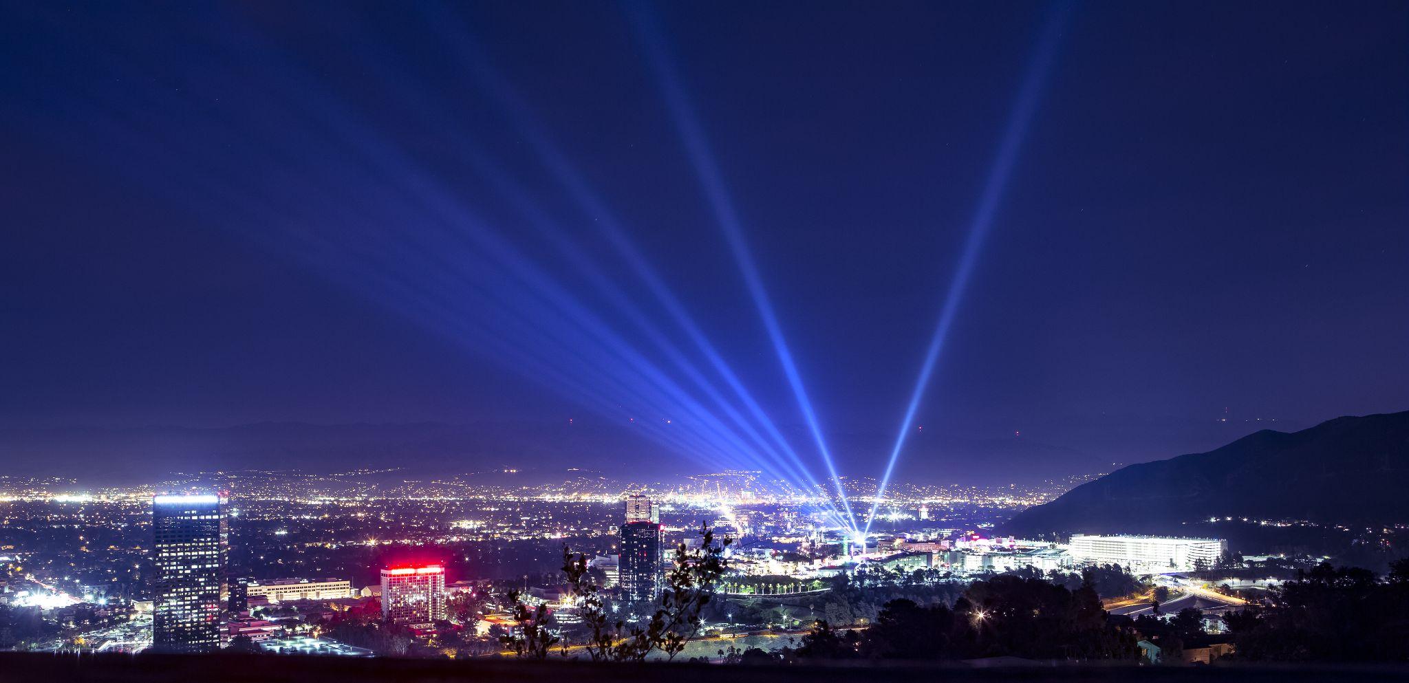 Huge bright powerful spotlight rays over the night sky panorama of Los Angeles city from Hollywood Hills